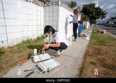 A volunteer team of Asian American teen girls repaints outdoor walls in a slum of Stanton, California, as part of a cleanup campaign. Stock Photo