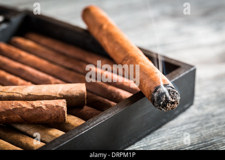 Burning cigar with smoke on old humidor Stock Photo