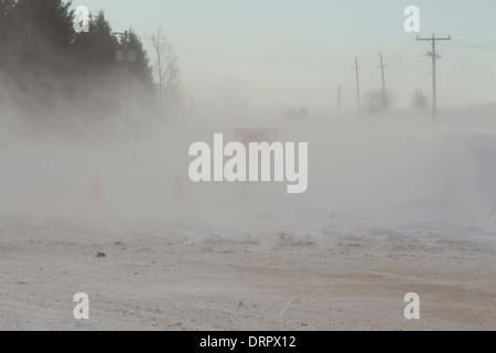 A road closure sign blocks a roadway after vehicles become trapped in wind blown winter snow & severe winter blizzard conditions Stock Photo