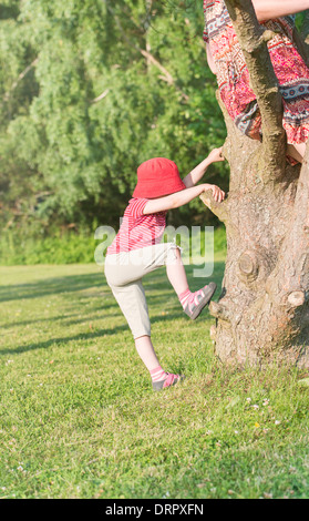 Tranquil summer scene. Young girl in green park climbing with mother up in the tree. Stock Photo