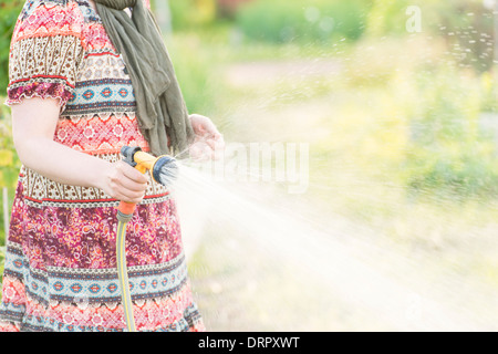 Lifestyle summer scene. Woman watering garden plants with sprinkler. Stock Photo