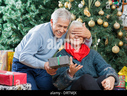 Senior Man Surprising Woman With Christmas Gifts In Store Stock Photo