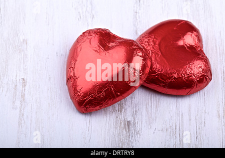 Chocolate hearts wrapped in red foil on a light painted wooden background Stock Photo
