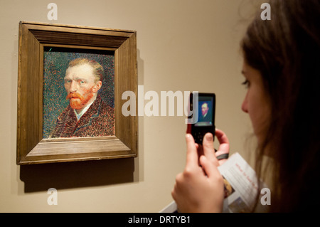 A pretty brunette girl takes a picture of 'Self-Portrait', by Vincent van Gogh, in The Art Institute of Chicago art museum. Stock Photo