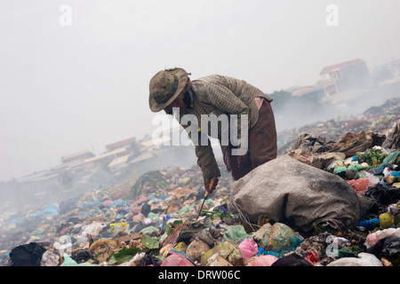 A scavenger woman is using a gaff to collect soft plastic at the toxic Stung Meanchey Landfill in Phnom Penh, Cambodia. Stock Photo