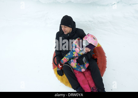Father and daughter having fun in snow inner tube - snowtubing Stock Photo