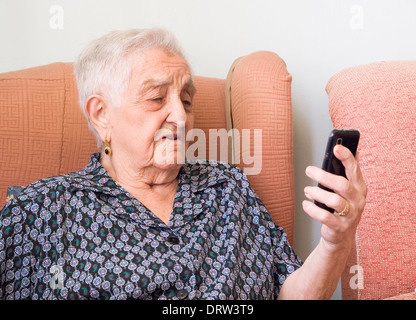 Elderly woman looking at a smartphone with confused expression. The woman is in her home. Stock Photo