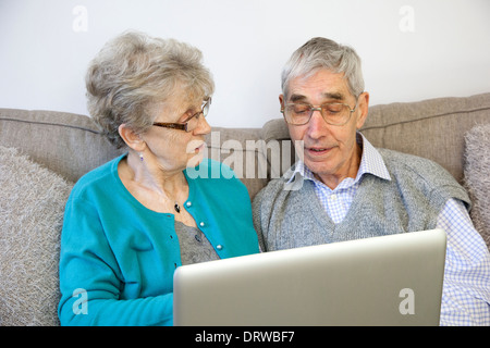 Senior couple sitting using a laptop at home. Stock Photo