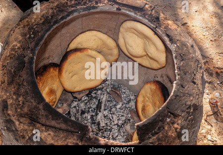 Flatbreads cooking on inside walls of an outdoor Tandoor oven, Tunisia. Stock Photo