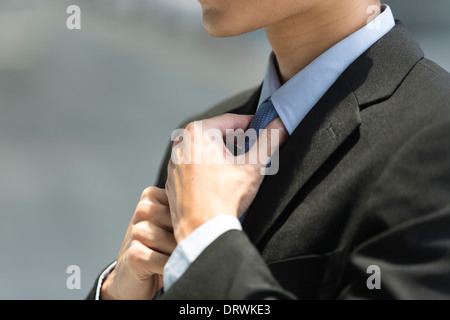 Close up detail of an Asian business man wearing a suit and adjusting his blue tie. Stock Photo