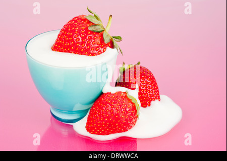 Three strawberries in blue cup with yogurt spill on a pink background Stock Photo