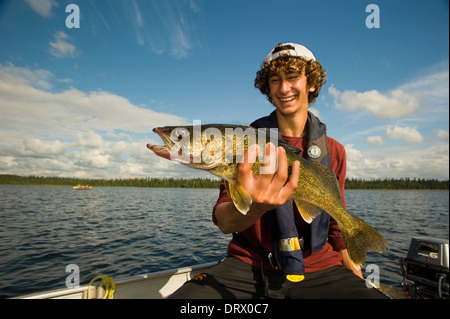 A young angler holds up a summer walleye in his motor boat. Stock Photo