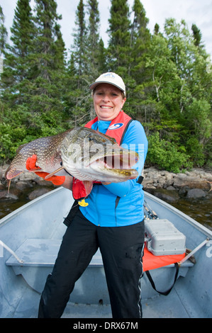 Woman angler trying to hold up a huge northern pike she caught from a boat on a lake in Northern Ontario, Canada Stock Photo
