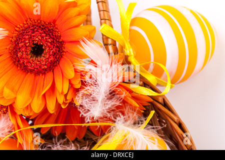 Colourful yellow hand decorated traditional Easter eggs with stripes and polka dot patterns arranged with colourful orange Gerbera daisies a decorative ribbon, on white with copyspace Stock Photo