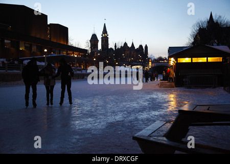 Three silhouettes skate along the Rideau canal in Ottawa, Ontario, Canada, the city and parliament buildings in the background. Stock Photo