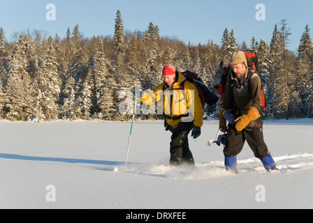 Two people snowshoe across a frozen lake in winter. Stock Photo