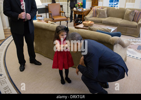 US President Barack Obama bends down to listen to the daughter of a departing U.S. Secret Service agent in the Oval Office of the White House October 28, 2013 in Washington, DC. Stock Photo