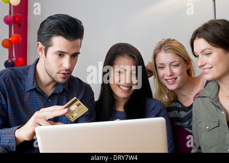 Friends gathered around laptop computer preparing to use credit card for online purchase Stock Photo