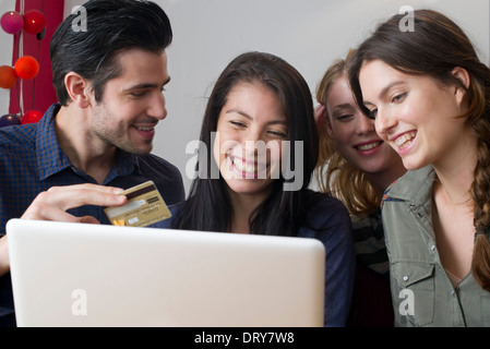 Friends gathered around laptop computer preparing to use credit card for online purchase Stock Photo