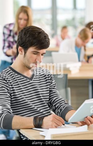 Male student writing notes in classroom Stock Photo