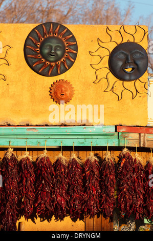 Dried peppers and art displayed against an adobe structure lit by late afternoon sun. Stock Photo