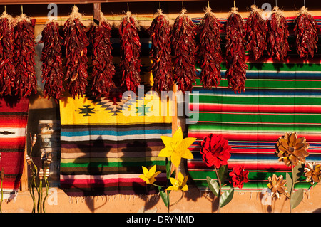 Dried peppers, rugs and art displayed against an adobe structure and lit by late afternoon sun. Stock Photo