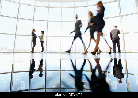 Several white collar workers communicating in office against window with three colleagues walking through near by Stock Photo