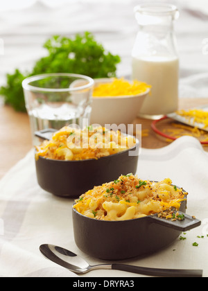 Two servings of baked macaroni and cheese with parsley garnish, a bowl of cheese and a glass of milk in the background.