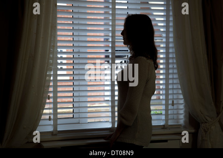 Silhouette of woman standing by a window. Over shoulder back/side view. Stock Photo