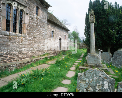 St Issui's church, Partrishow, Powys: churchyard preaching cross opposite stone benches running alongside chancel & nave. Paved Public footpath. Stock Photo