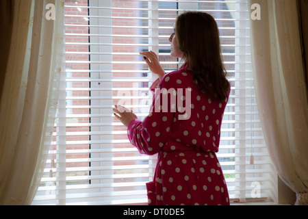 Silhouette of woman wearing a dressing gown looking out of a window. Over shoulder back/side view. Stock Photo
