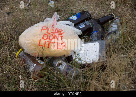 Empty glass bottles and other trash in a 'Please don't litter' plastic bag on ground at a rest stop in rural south Texas. Stock Photo