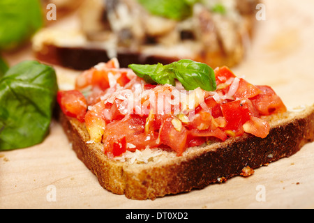 Closeup of tomato bruschetta decorated with basil and cheese on a wooden board Stock Photo