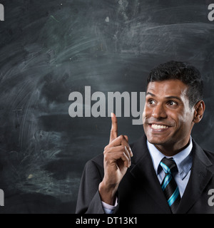 Indian business man standing next to a blackboard & pointing upwards. Stock Photo