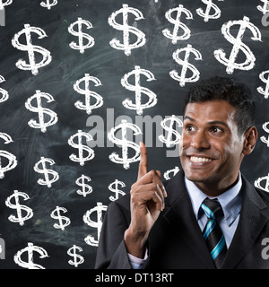 Happy Indian Business man pointing at dollar signs on a chalk board. Stock Photo