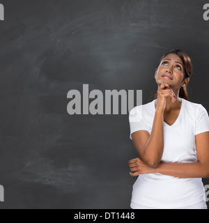 Happy Asian woman standing in front of a dark chalkboard. The chalk board is blank waiting for a message. Stock Photo