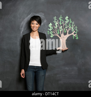 Happy Asian Business woman in front of chalk money tree drawing on blackboard. Stock Photo