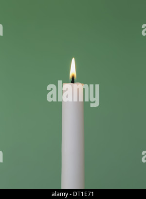 thin white wax candle with small lit flame Stock Photo