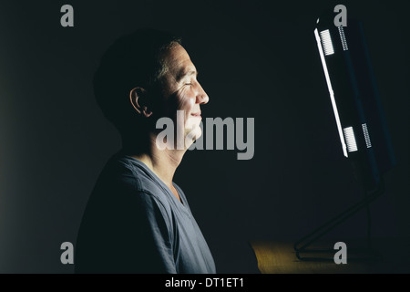 Smiling middle aged man sitting in front of a light therapy box treatment of suffering from seasonal affective disorder Stock Photo