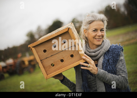 Organic Farmer at Work A woman holding a bug box a wooden box with holes for insects to nest in Stock Photo