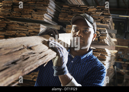 heap of recycled reclaimed timber planks of wood Environment timber yard A man carrying a large plank of splintered rough wood Stock Photo