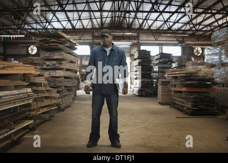 A heap of recycled reclaimed timber planks of wood reclamation in a timber yard A man in work overalls with a clipboard Stock Photo