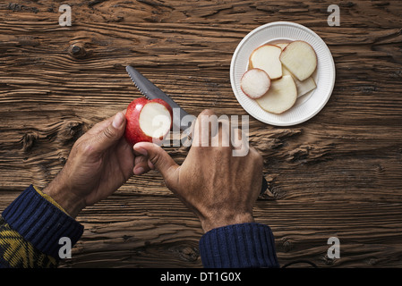 A person holding and slicing sections of a red skinned apple Stock Photo