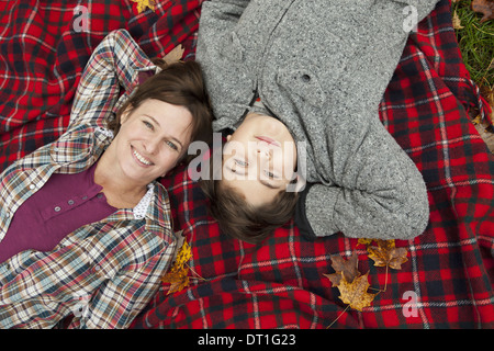 Two people a woman and a child lying on a red tartan picnic blanket looking upwards Stock Photo