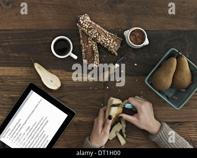 A person using a peeling knife to peel a pear A computer tablet device with the screen displaying instructions a recipe Stock Photo