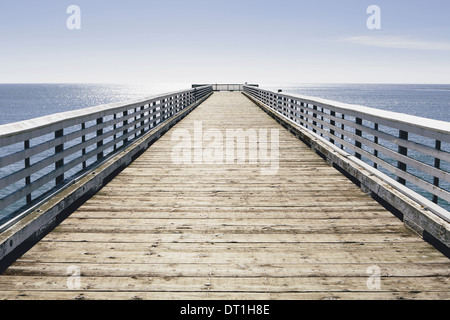 A long pier with railings extending out over the Pacific Ocean leading to the horizon Stock Photo