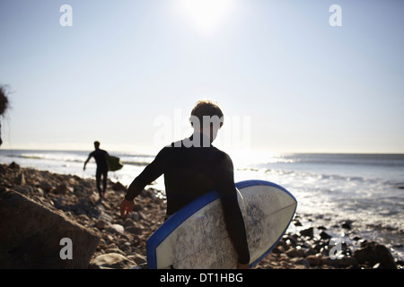 Two people in wetsuits on a beach carrying their surfboards Stock Photo