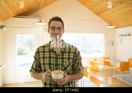 A young man standing holding a cup of coffee in a coffee shop Stock Photo