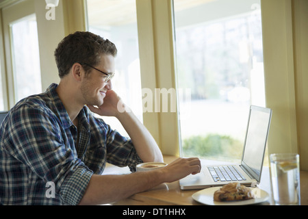 A young man sitting at a table using a laptop computer Stock Photo