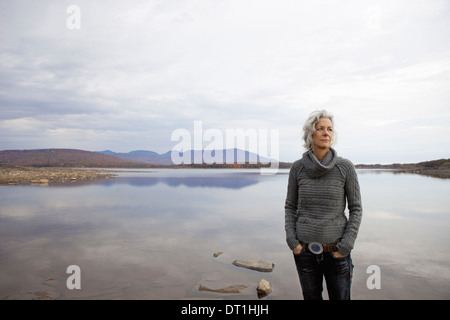 A woman looking out over the water on the shores of a calm lake Stock Photo